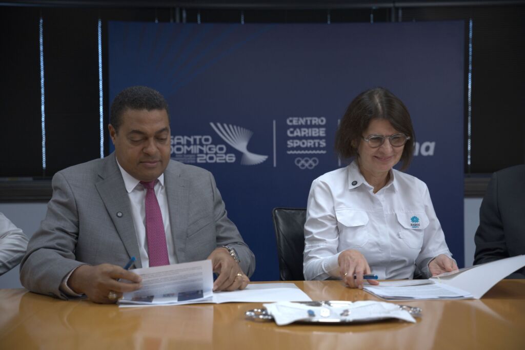 José P. Monegro y Mercedes Ramos se disponen a firmar el acuerdo entre el Comité Organizador de los Juegos Santo Domingo 2026 y el Grupo Ramos, patrocinador oficial del evento multideportivo internacional.