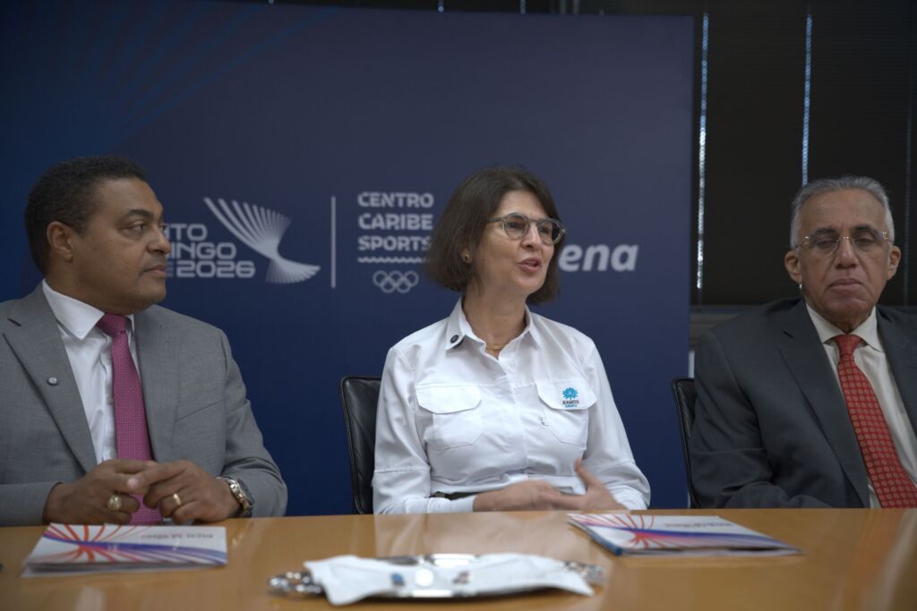 Mercedes Ramos habla durante el acto de firma del acuerdo de patrocinio entre el Grupo Ramos y el Comité Organizador de los Juegos Centroamericanos y del Caribe Santo Domingo 2026. A la izquierda, José P. Monegro y a la derecha, Luisín Mejía.